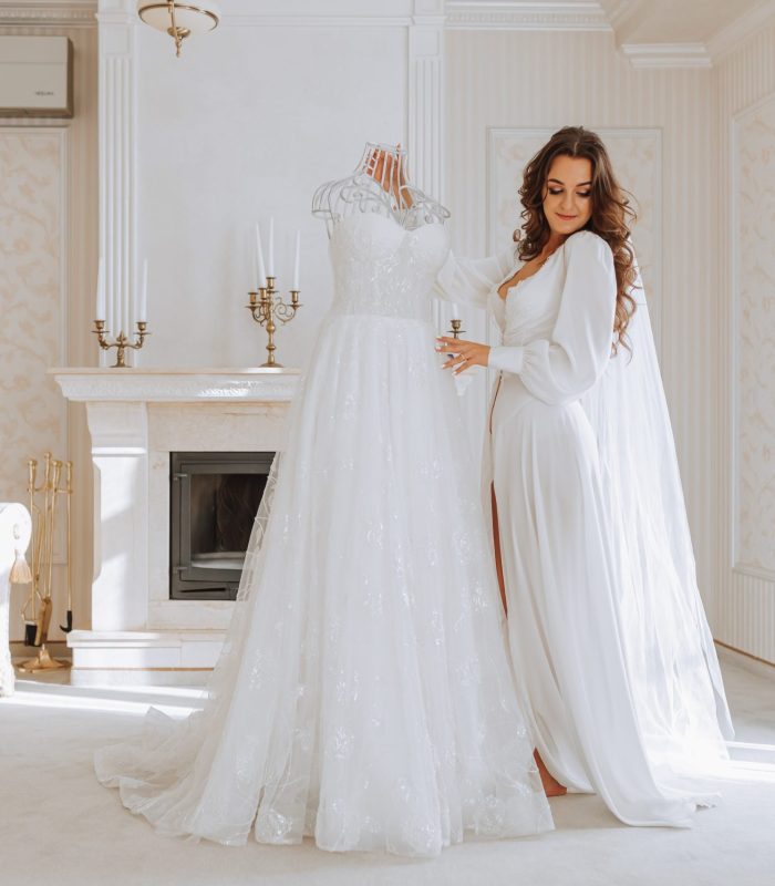 young curly girl with long hair in luxurious room standing near her dress on maeken white open dress getting ready for wedding ceremony